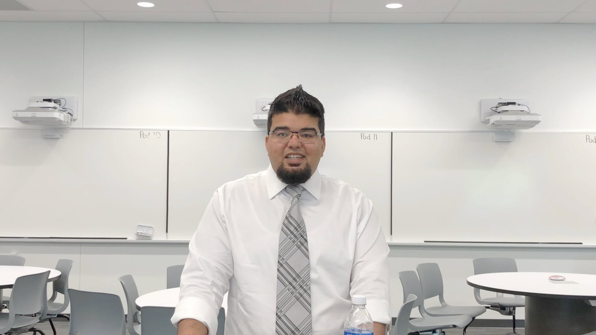 Kamran seated in a mathematics classroom in front of a whiteboard, wearing a white shirt and tie